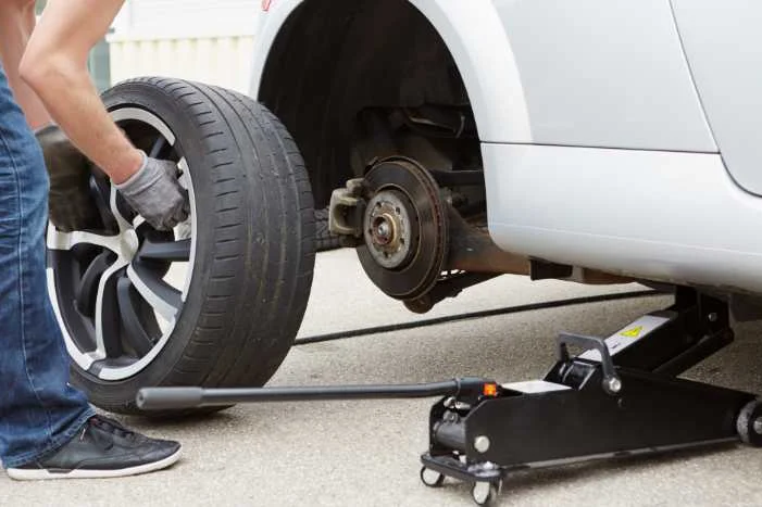 Person wechselt einen Autoreifen mit Wagenheber.